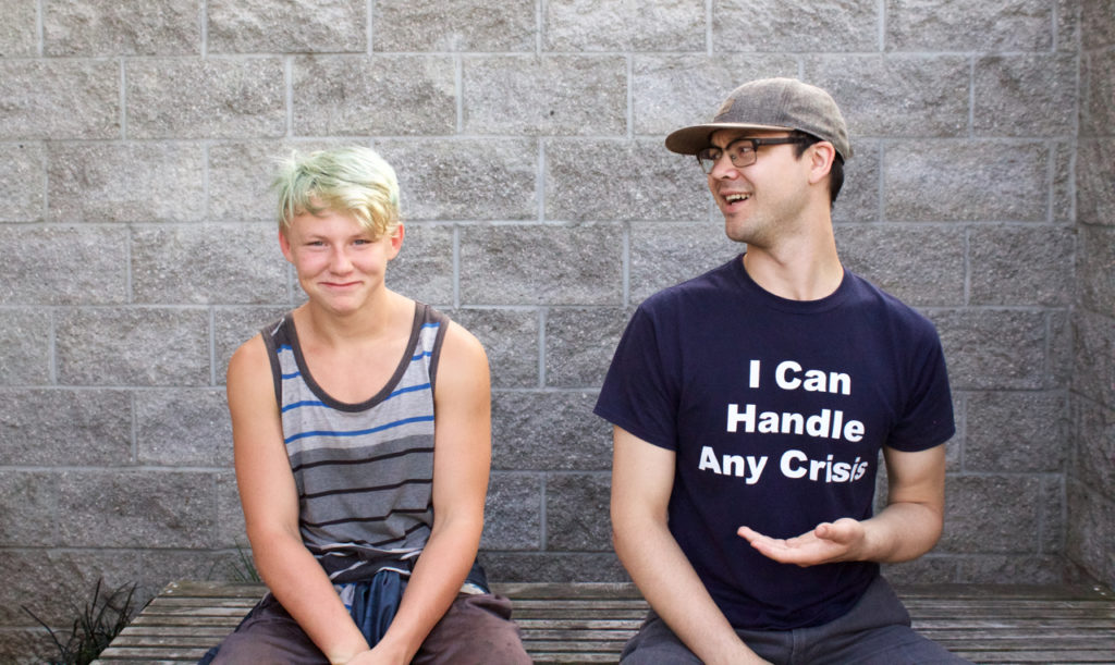 Youth on the left, staff on the right in a shirt that says I can handle any crisis. Youth is smiling while staff member is smiling at the youth. 