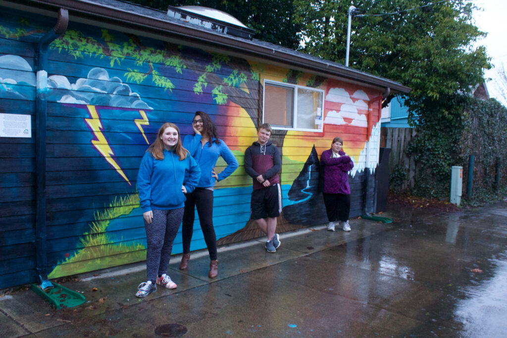 Youth standing in front of a mural they created. 